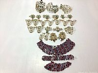 Full overview of gold-tone filigree jewelry parts and red crystal rhinestone strips laid on white background