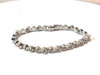 Photo of a white rhodium tennis bracelet with clear Swarovski crystals linked in a continuous line, the bracelet forms a circle on a white background.