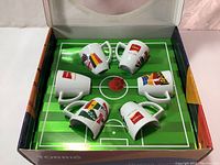 Six espresso coffee cups with colorful World Cup flags arranged inside the box on a soccer field themed interior