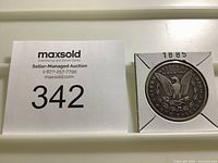 Full view of 1885 Morgan Dollar coin in paper holder with year labeled