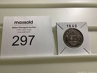 Close-up photo of the coin in its holder labeled '1940' beside a MaxSold auction label with lot number 297.