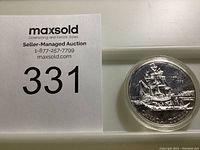 Full lot view showing coin in protective casing next to MaxSold auction lot tag '331'.