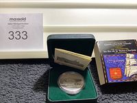 Proof silver dollar coin in green velvet case alongside certificate and box with anniversary details.