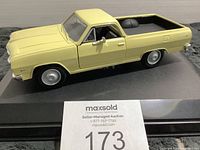 Front and side view of yellow Chevrolet El Camino collectible model vehicle on display base, shows closed driver side door and tire detail.