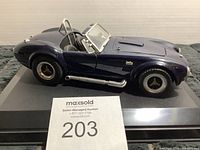 Side view of dark blue metallic Shelby Cobra 427 diecast model on black display base.