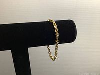 Gold-tone bracelet displayed on black bracelet stand showing interlinked chain and stone pattern.