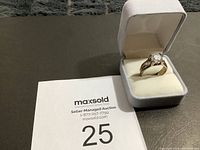 Estate ring displayed in a white cushioned jewelry box alongside a number card with auction information.