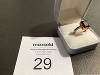 Ring displayed in a light grey velvet box with a large rectangular black stone and side row of clear stones.