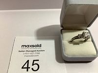 Estate ring with a clear central stone and smaller stones on a silver-tone band, displayed in a gray padded jewelry box with cream interior.