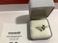 Ring with purple teardrop-shaped stone set in sterling silver band inside grey padded jewelry box