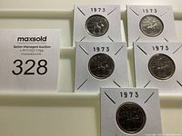 Five 1973 Canadian quarter dollars with RCMP design arranged in a tray, each coin in a cardboard holder stamped '1973'.
