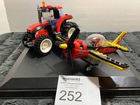 Photo showing both the red tractor and yellow airplane models together from an angled side view on a black surface.