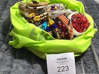 Photo showing large mixed collection of costume jewelry with several colorful beaded bracelets, bangles, and necklaces in a green fabric container.
