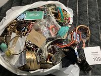 Photo of a large mixed collection of costume jewelry in a white bag including bangles, beaded necklaces, and assorted bracelets and earrings with mixed colors and materials