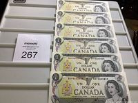 Six sequentially numbered 1973 Canadian $1 bills laid flat on a tray showing front side with Queen Elizabeth II portrait and coat of arms.