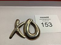 Front view of silver XO brooch showing smooth, rounded shape and polished surface.
