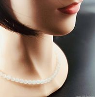 Close-up of the necklace worn on a mannequin neck showing the white jade bead necklace in a single strand.