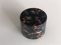 Top view of the herb grinder showing the black and orange decorative exterior pattern, in a closed position.