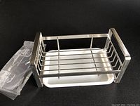 Top-front view of the stainless steel kitchen sponge holder resting on its white drip tray, showing the metal frame and overall condition.