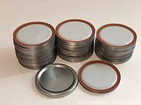 Stack of metal regular mouth canning lids with orange silicone sealing rings on edges