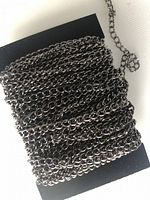 Coiled black iron twisted flat cross chains on black card background showing the flat, interlocking twisted cross pattern.