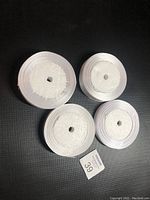 Four rolls of white satin ribbon on foam cores, shown from top to display the wound ribbon ends and approximate widths.