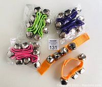 Four sets of ankle and wrist bells on colored straps, three sets individually packaged: green, purple, and pink; one orange strap with bells unwrapped.