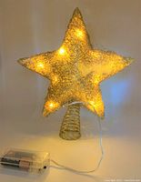 Gold star shaped tree topper illuminated by integrated lights with battery pack attached.