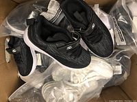 Box of black Skechers runners on top of multiple pairs in packaging including white color