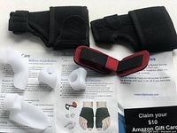 All kit components laid out on informational pamphlet including two black fabric bunion corrector splints and multiple white gel toe separators