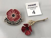 Three poppy pins: large enamel 'Lest We Forget' pin, smaller red enamel poppy, and gold-tone stem brooch