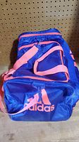 Photo of purple and pink Adidas gym bag showing front zippered pocket with Adidas logo and pink straps.