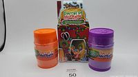 Front view of orange and purple Barrel of Monkeys candy cane edition barrels with box behind them