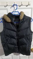 Front view of the black padded vest with faux fur collar hanging on a blue hanger.