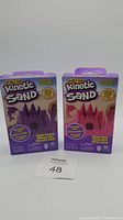 Two boxes of Kinetic Sand, one neon purple and one neon pink, placed side by side.