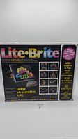 Front of the Lite Brite Ultimate Bonus Edition box showing colorful logo, pegboard with dinosaur design, and glowing pegs description.