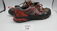 Side view of one Merrell men's trail shoe, showing black, red, and gray colors with Vibram sole branding on heel.