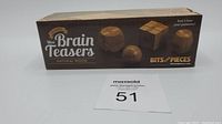 Box front showing Classic Mini Brain Teasers natural wood, Bits and Pieces branding, image of puzzles, and lot number card