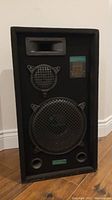 Front view of Grafdale Pro Series speaker showing woofer, midrange, and tweeter drivers with metal grills and fabric-covered enclosure on hardwood floor.