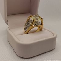 Close-up angled side view of the gold-tone ladies ring with CZ and rhinestones in a white ring box, showing detailing and stone placement.