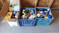 Wide view of three boxes filled with various household and commercial cleaning liquids, sprays, and powders.