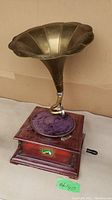 Side angled view of the gramophone showing the wooden base, purple fabric covered turntable plate, brass horn, and hand crank.