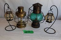 Four items displayed on table: two vintage oil lamps and two black metal candle holders with hanging crystals.