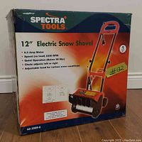 Front view of boxed Spectra Tools 12 inch electric snow shovel showing product image and features like 6.5 amp motor, chute adjustments, and 1 year warranty.