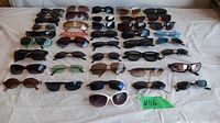 Top view of 26 assorted sunglasses arranged on a white surface showing variety of frame and lens styles and colors