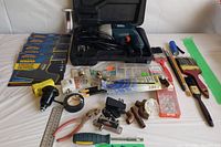 Photo of entire lot including Black & Decker drill, power scraper attachments, copper pipes, paint brushes, pliers, and other small tools arranged on white surface.