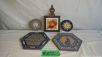 Full lot, showing all 5 items including 2 hexagonal tiles, cast iron trivet with painted tile insert, and 2 round sun wall decorations.