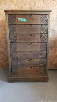 Front view of seven drawer wooden cabinet with carved decorative panels on each drawer.