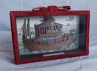 Side angled view of the Noah's Ark shadowbox art inside the red velvet frame showing the three-dimensional woodcut ark with animals and background waves and birds.