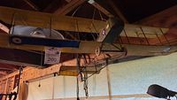 Full side view of the model biplane showing olive green fuselage and tail with red, white, and blue markings, suspended from ceiling.